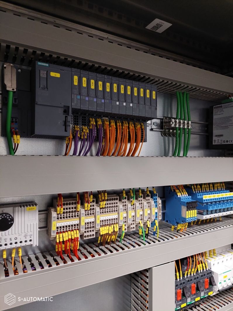 Szczegółowe ujęcie szafy sterowniczej z modułami Siemens, okablowaniem oznaczonym żółtymi etykietami i elementami zabezpieczającymi, widoczne przewody w kolorach zielonym, pomarańczowym i fioletowym.