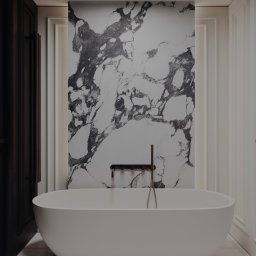 S STUDIO Sandra Kluczek - Nowoczesna łazienka z wolnostojącą białą wanną na tle ściany z motywem marmuru i złotą armaturą, obok ciemne, ozdobne drzwi.