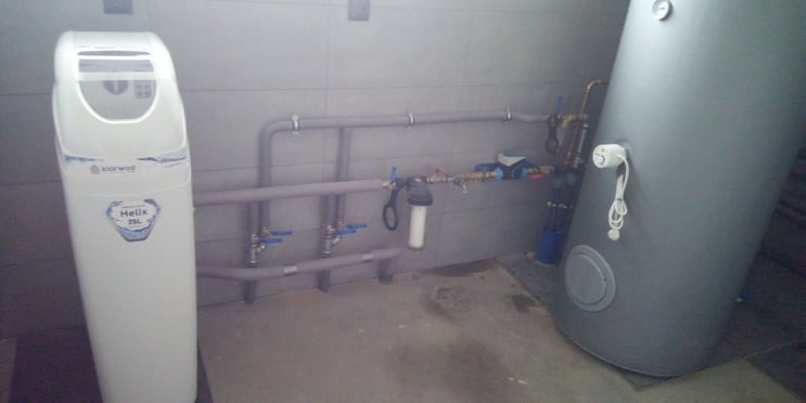 Instalacja uzdatniania wody Klarwod Helix 25L połączona z bojlerem i rurami w pomieszczeniu z szarymi płytkami.