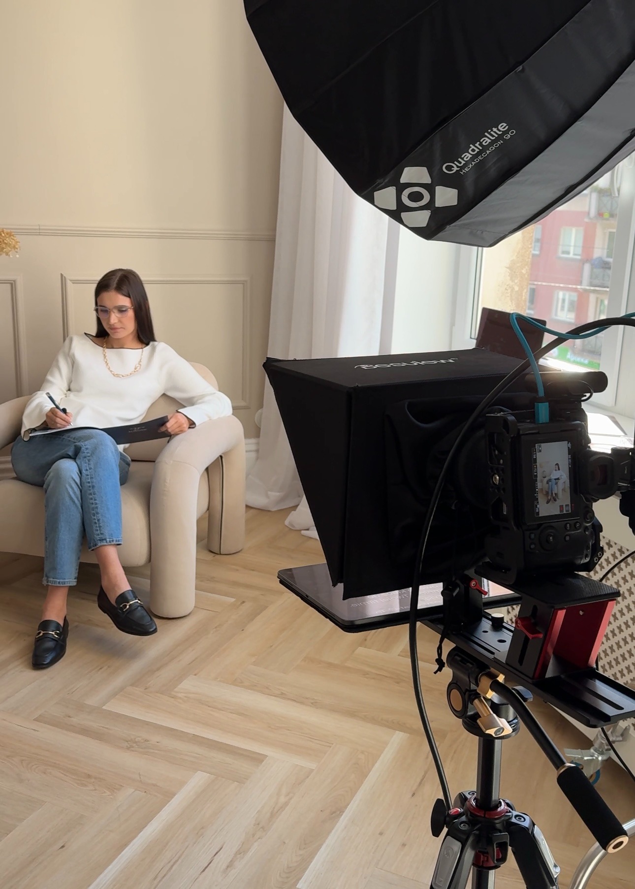 Kobieta w okularach siedząca w fotelu, pisząca na tablecie podczas sesji zdjęciowej z profesjonalnym oświetleniem i aparatem na statywie.
