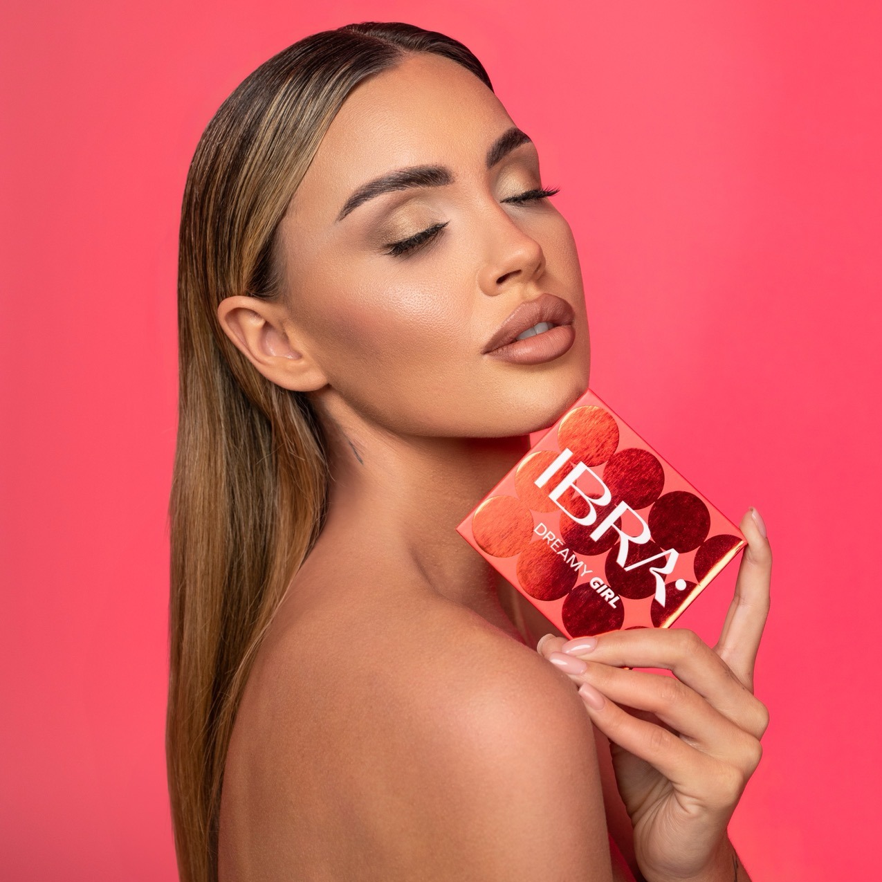 Portret kobiety z zamkniętymi oczami, prezentującej paletę cieni do powiek marki IBRA Dreamy Girl na tle intensywnego różu.
