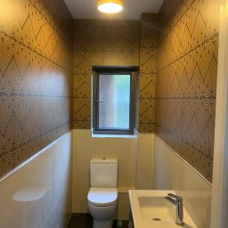 LW DECOR - ŁUKASZ WYMYSŁOWSKI - Wąska łazienka po remoncie z toaletą, umywalką na szafce i wzorzystą tapetą w stylu retro na górnej części ścian.