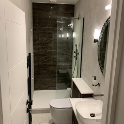 LW DECOR - ŁUKASZ WYMYSŁOWSKI - Nowoczesna łazienka z kabiną prysznicową typu walk-in, umywalką nablatową i dużym owalnym lustrem, wykończona szarymi płytkami i akcentami z ciemnego marmuru.