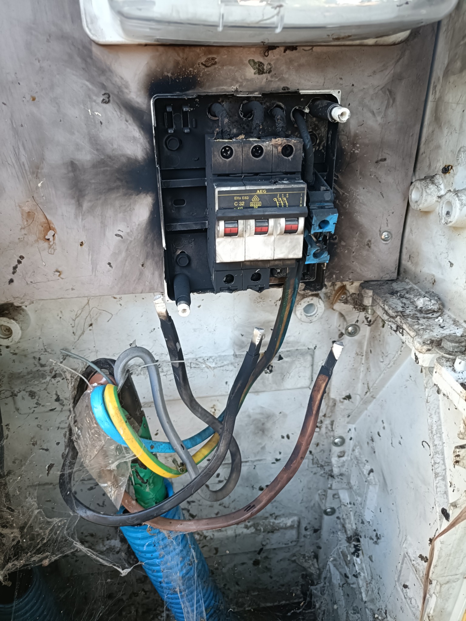 Uszkodzona skrzynka elektryczna w Chwaszczynie z przepalonymi bezpiecznikami i okopconymi ściankami, widoczne kable i ślady po zwarciu.