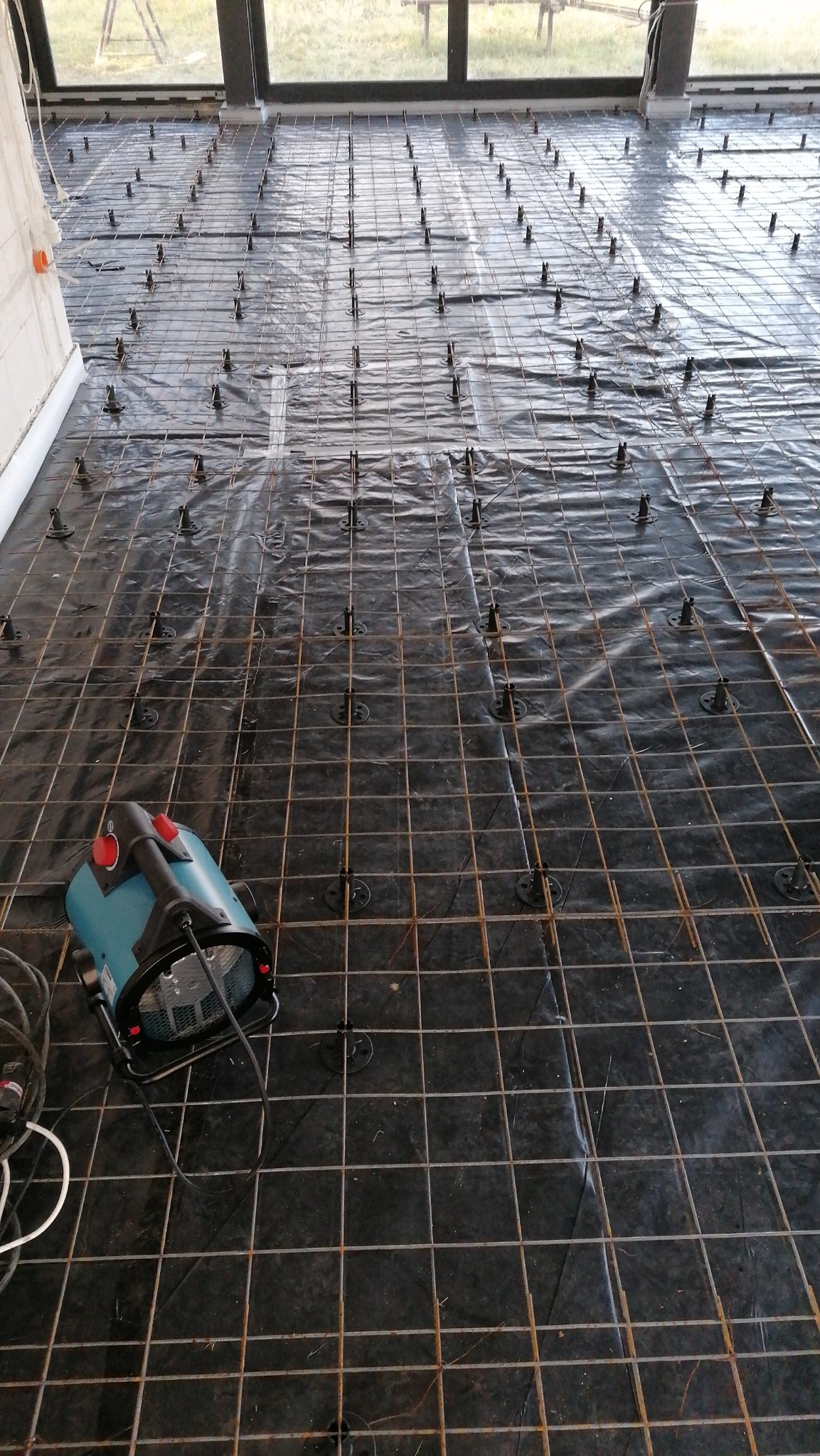 Przygotowanie podłoża pod wylewkę: siatka zbrojeniowa na folii z dystansami, nagrzewnica w rogu pomieszczenia.