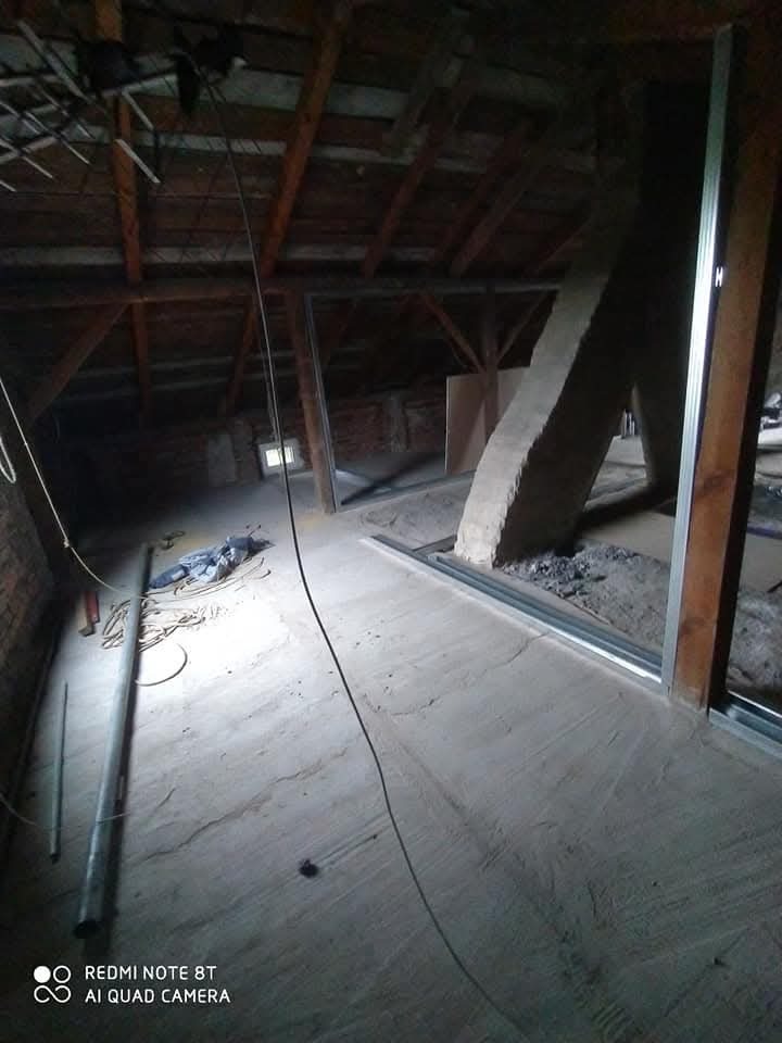 Poddasze w trakcie adaptacji: widoczne drewniane krokwie, metalowe profile konstrukcyjne, częściowo ocieplona przestrzeń oraz narzędzia pracy, przygotowane pod zabudowę karton-gipsem.