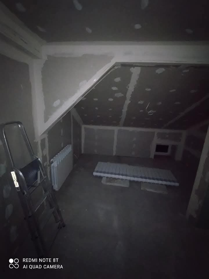 Poddasze w Skierniewicach w trakcie prac wykończeniowych: ściany i sufit pokryte płytami gipsowo-kartonowymi, widoczna drabina i grzejnik, przygotowane materiały budowlane na podłodze.