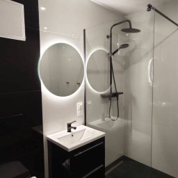 New House - Nowoczesna łazienka w tonacji czerni i bieli z okrągłym lustrem LED, czarną armaturą i kabiną prysznicową typu walk-in z odpływem liniowym w podłodze.