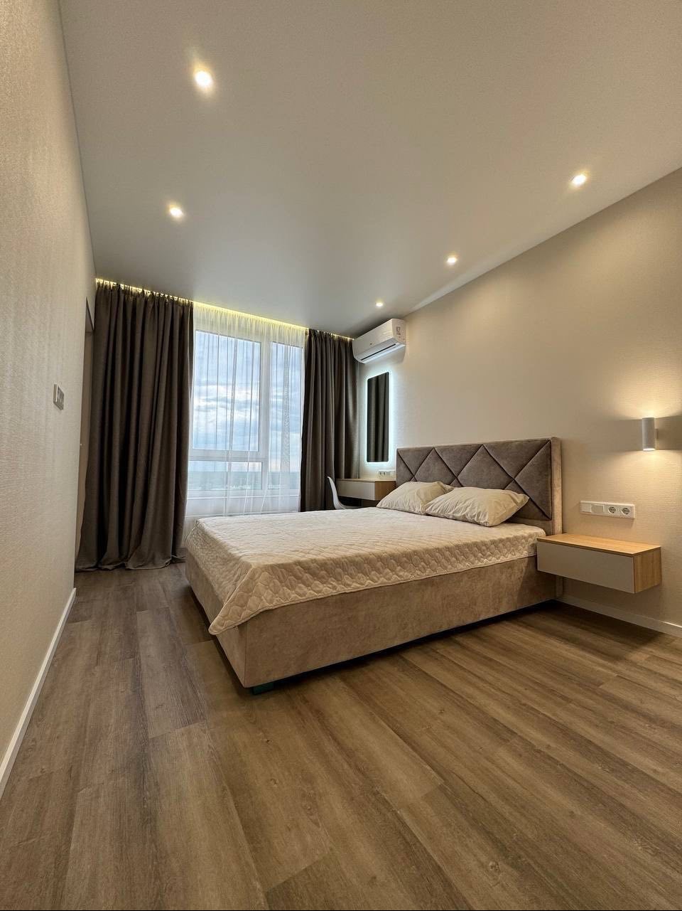 Nowoczesna sypialnia z łóżkiem z tapicerowanym zagłówkiem w romby, drewnianą podłogą i oknem z zasłonami.