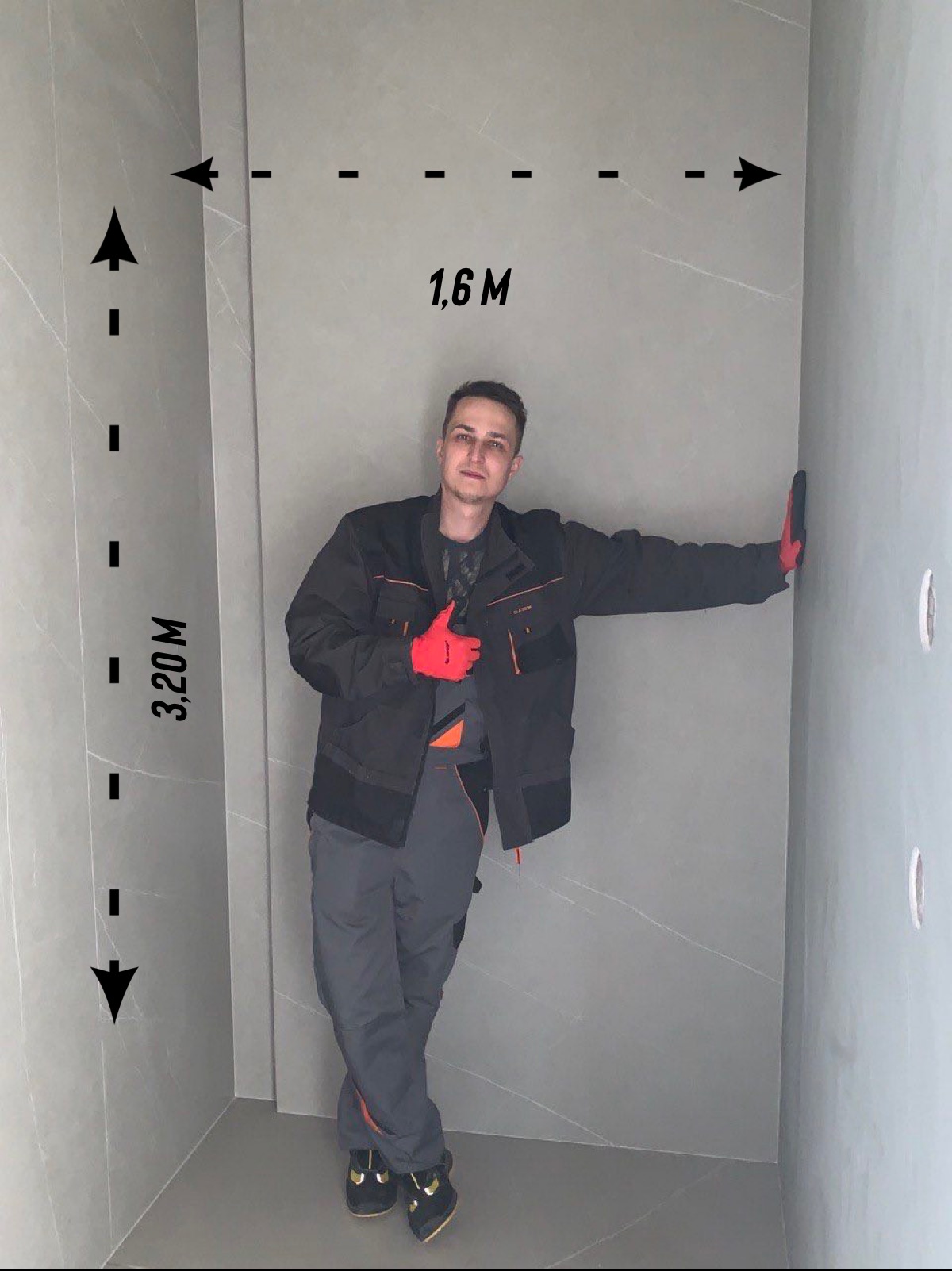 Mężczyzna w ubraniu roboczym prezentuje wykończoną łazienkę z szarymi płytkami imitującymi marmur, z naniesionymi wymiarami 1.6m x 3.2m na ścianach.