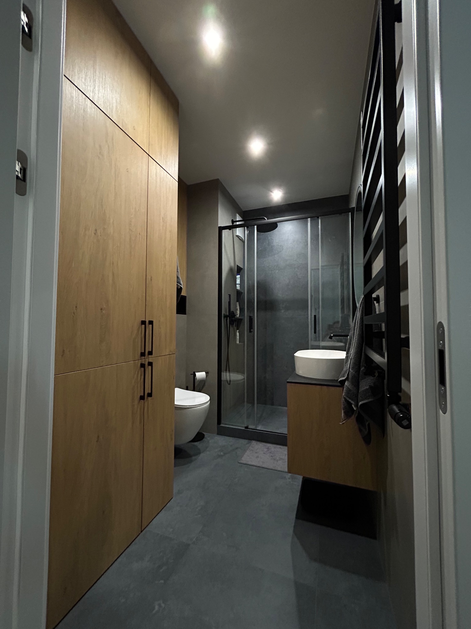 Nowoczesna łazienka z dużą, drewnianą szafą, kabiną prysznicową z czarną ramą i umywalką nablatową.