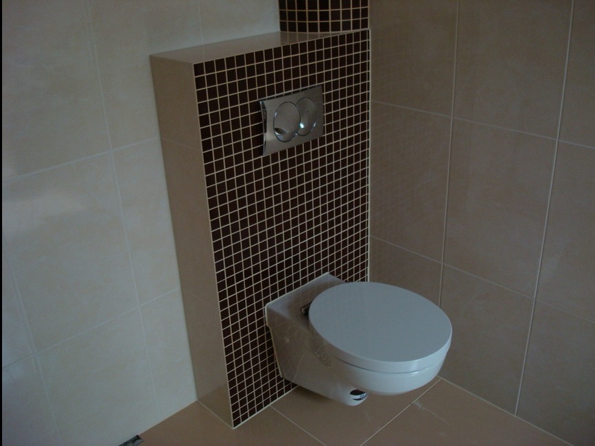 Podwieszana toaleta z zabudowanym stelażem, obłożonym brązową mozaiką, na tle beżowych płytek ściennych i podłogowych.