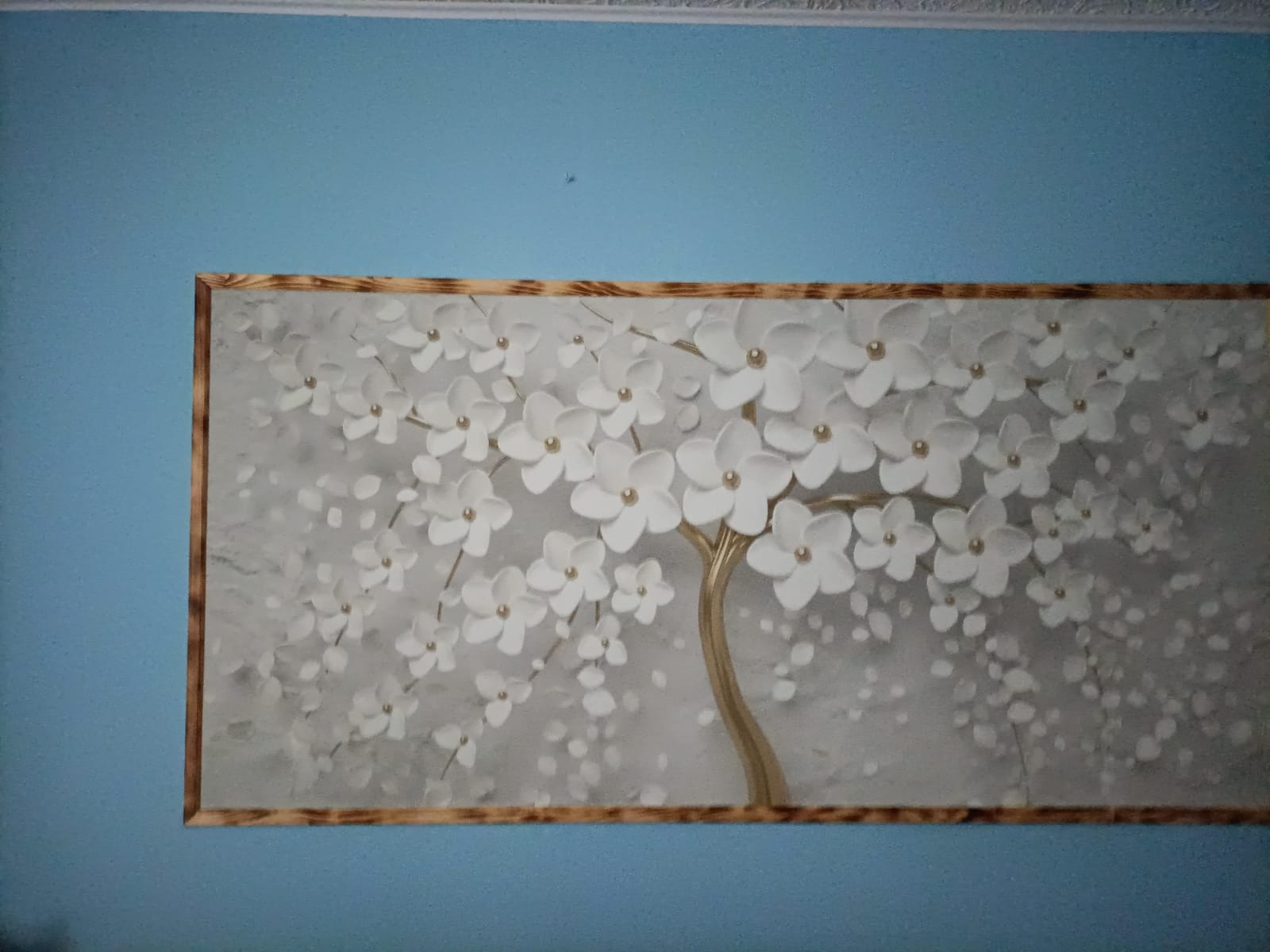 Tapeta z motywem kwitnącego drzewa z białymi kwiatami i złotym pniem, umieszczona na błękitnej ścianie.