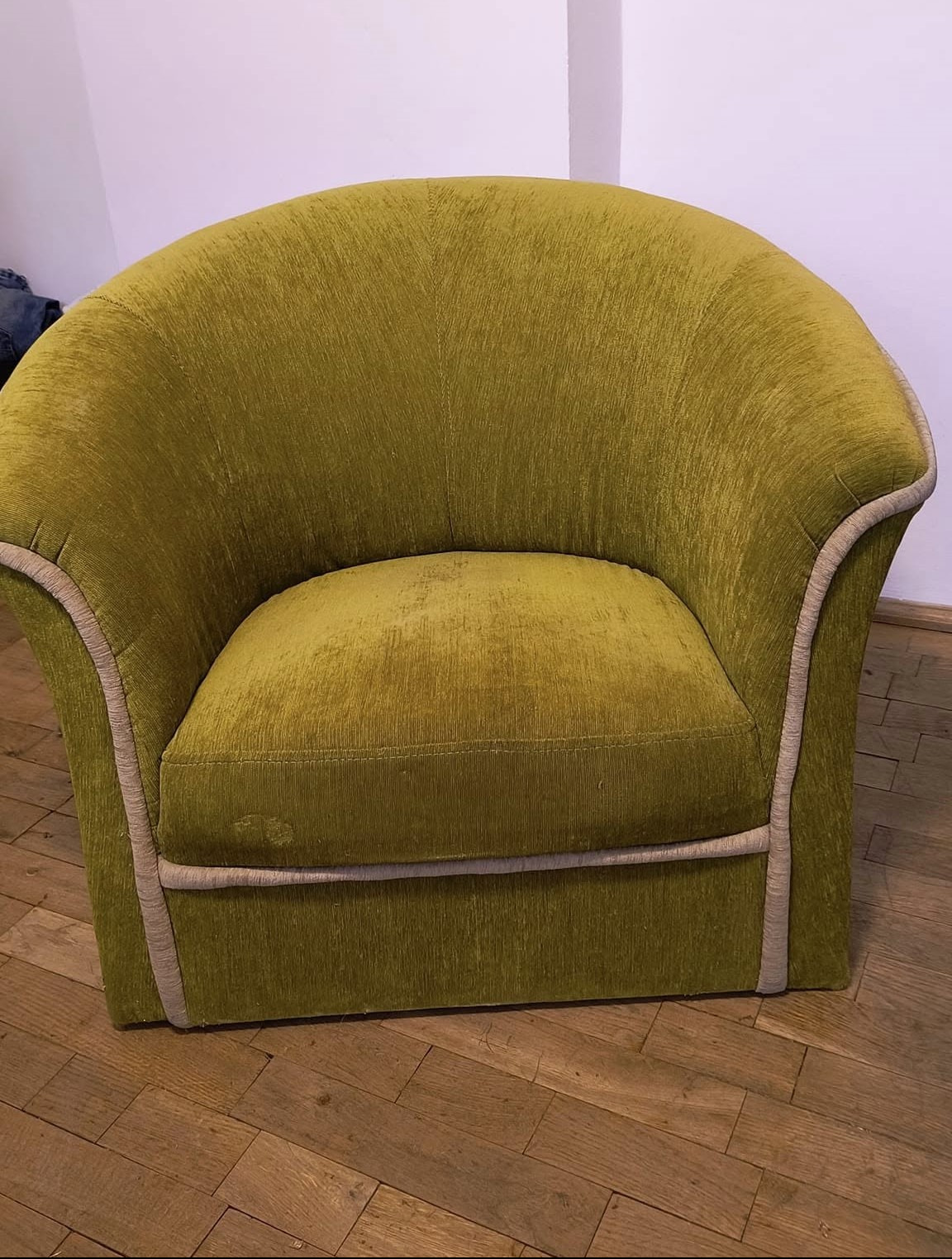 Krzesło obite zielonym pluszem z kremową lamówką, widoczne ślady użytkowania na siedzisku, na drewnianej podłodze.