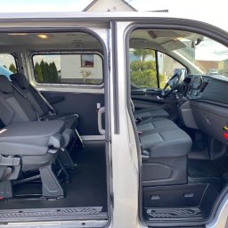 LUKIBUS WYNAJEM AUT Busa Nysa ŁUKASZ ŁOHIN - Wnętrze srebrnego busa z rozsuwanymi drzwiami, widoczne fotele pasażerskie z regulacją, deska rozdzielcza i gaśnica.