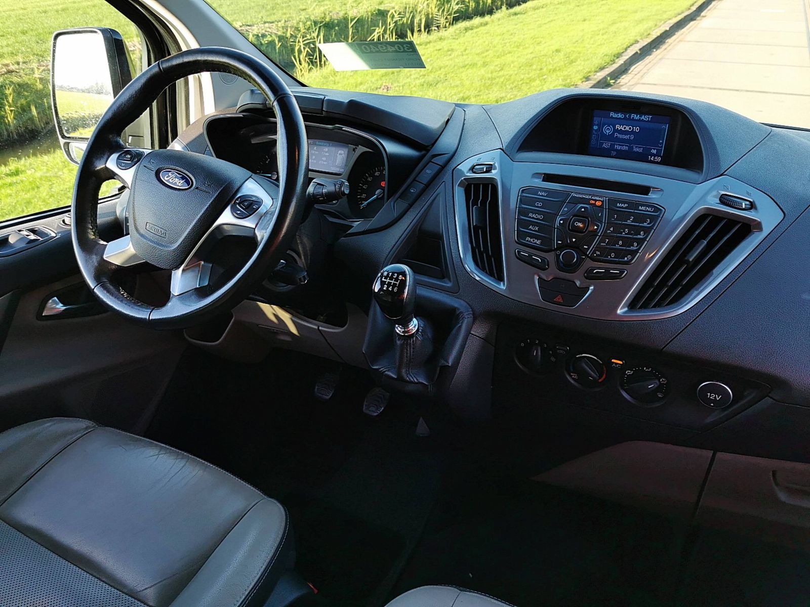 Wnętrze samochodu dostawczego marki Ford z widoczną deską rozdzielczą, kierownicą, fotelem kierowcy i dźwignią zmiany biegów.