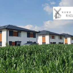 LUNA Sandra Siebert - Nowoczesne, dwukondygnacyjne domy szeregowe z ciemnymi dachami i roletami, widoczne zza pola kukurydzy w słoneczny dzień, logo dewelopera w prawym górnym rogu.