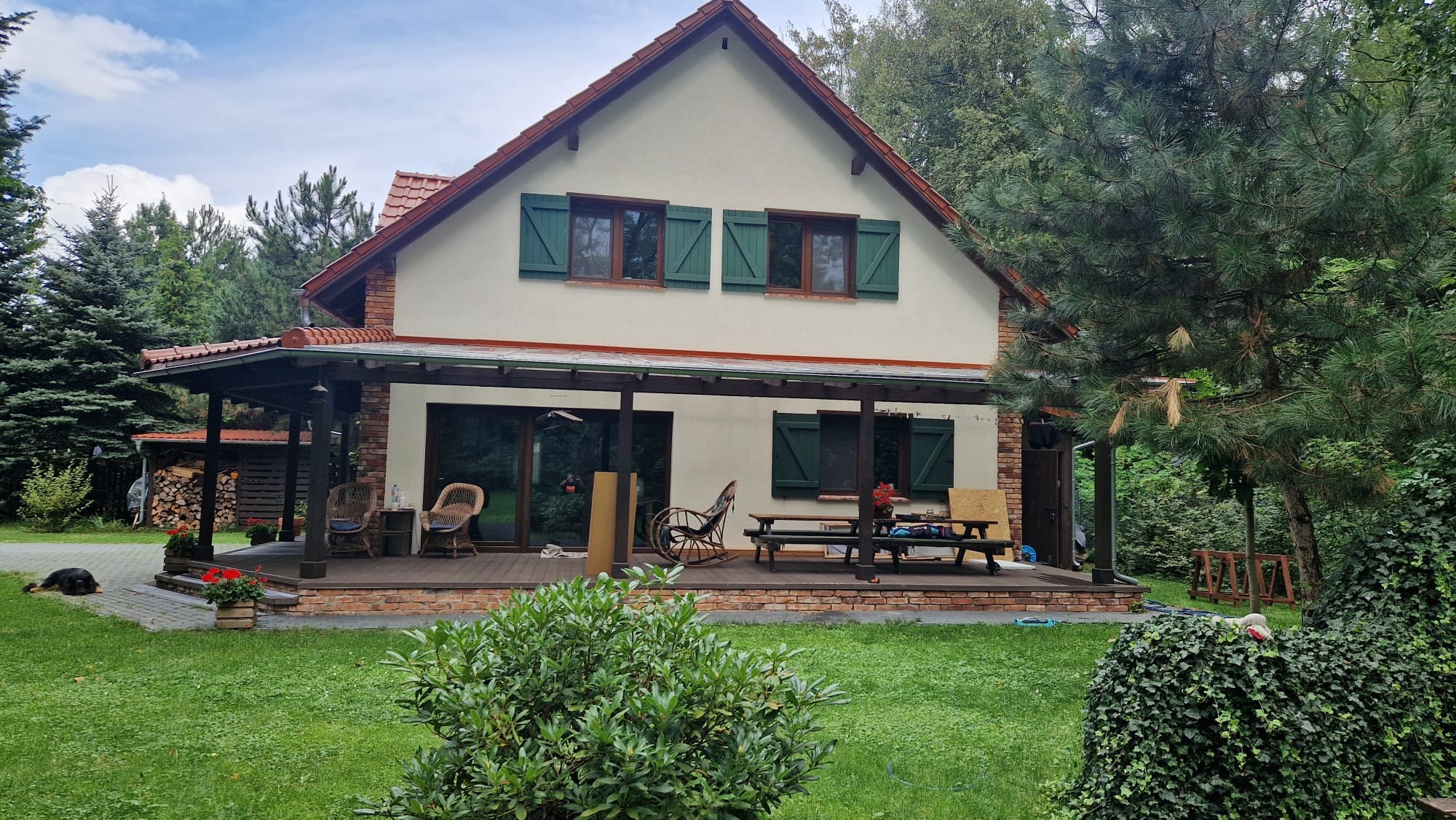 Dom jednorodzinny z werandą i zielonymi okiennicami, widok z ogrodu w pochmurny dzień.