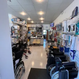 Wnętrze sklepu z artykułami medycznymi: w&oacute;zki inwalidzkie, balkoniki, ortezy i inny sprzęt rehabilitacyjny na p&oacute;łkach i wzdłuż ścian.