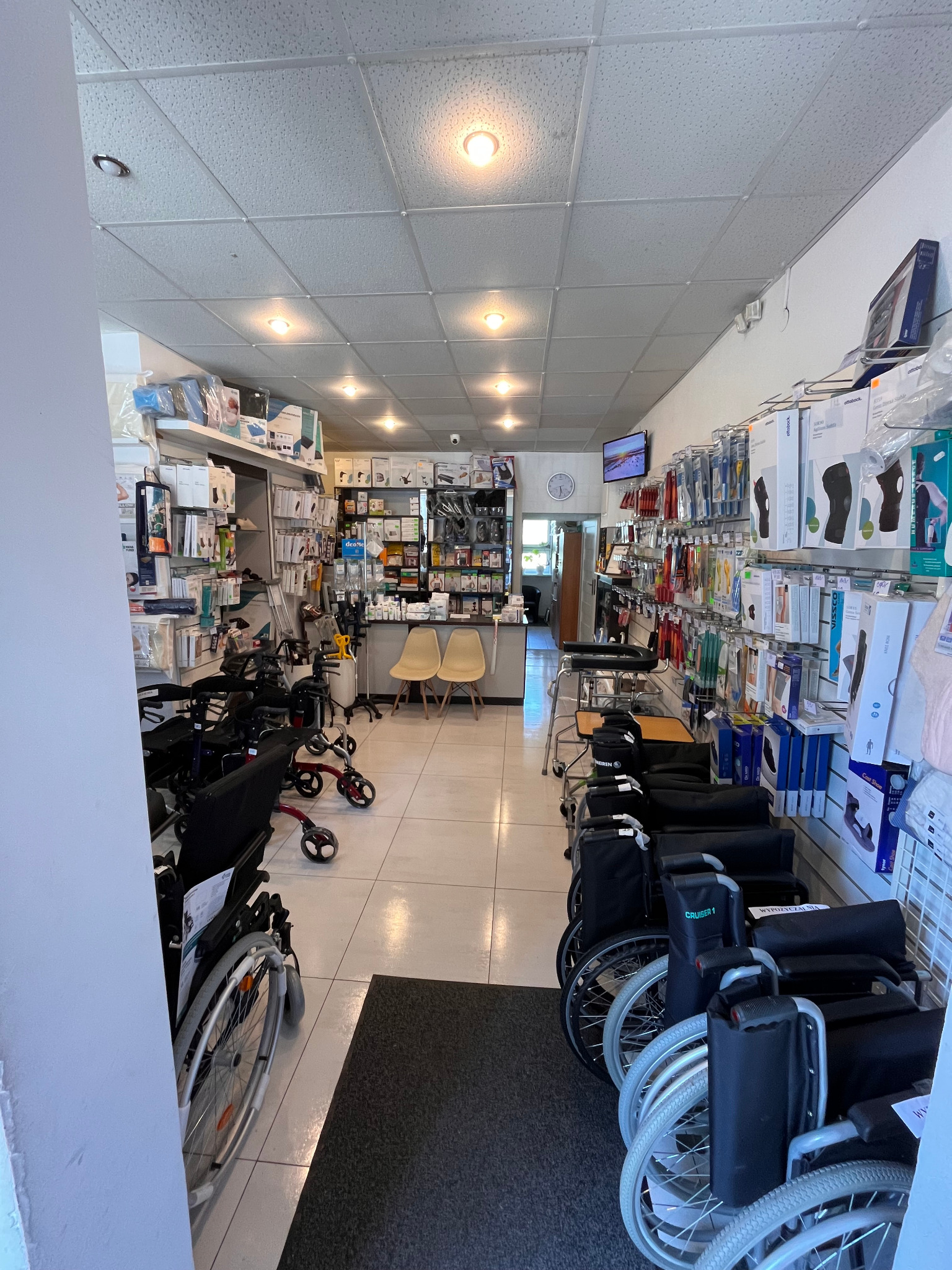 Wnętrze sklepu z artykułami medycznymi: wózki inwalidzkie, balkoniki, ortezy i inny sprzęt rehabilitacyjny na półkach i wzdłuż ścian.