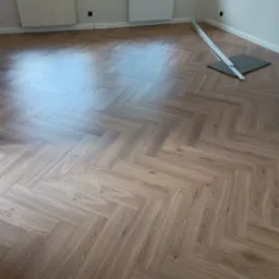 Ułożony parkiet w jodełkę francuską w Radomiu, z widocznymi listwami przypodłogowymi i narzędziami do montażu, jasne wnętrze z oknami.
