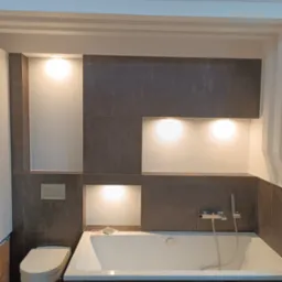 Nowoczesna łazienka z wanną, szarą okładziną i podświetlanymi wnękami. Minimalistyczny design, armatura chromowana, widoczny fragment toalety.