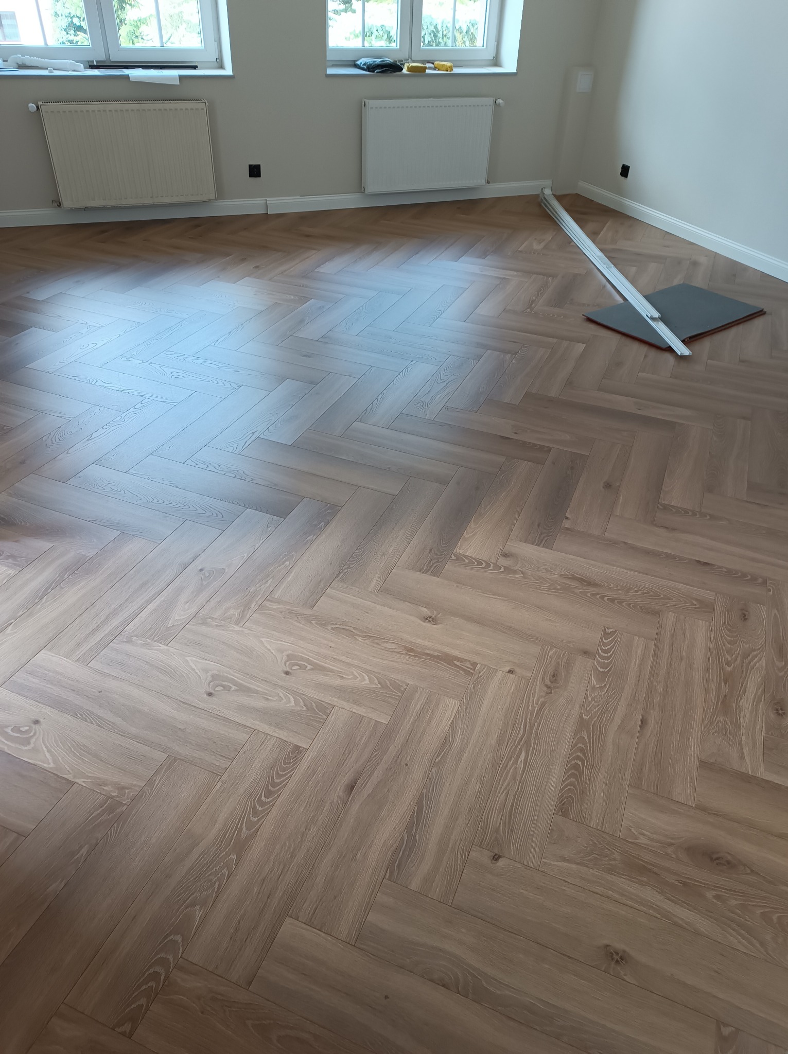 Ułożony parkiet w jodełkę francuską w Radomiu, z widocznymi listwami przypodłogowymi i narzędziami do montażu, jasne wnętrze z oknami.