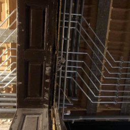 Rafał Jarząbek Rafinstal - Szczegółowe ujęcie instalacji rur w pomieszczeniu w trakcie remontu, widoczne drewniane elementy konstrukcyjne i stara, ciemna futryna drzwiowa.