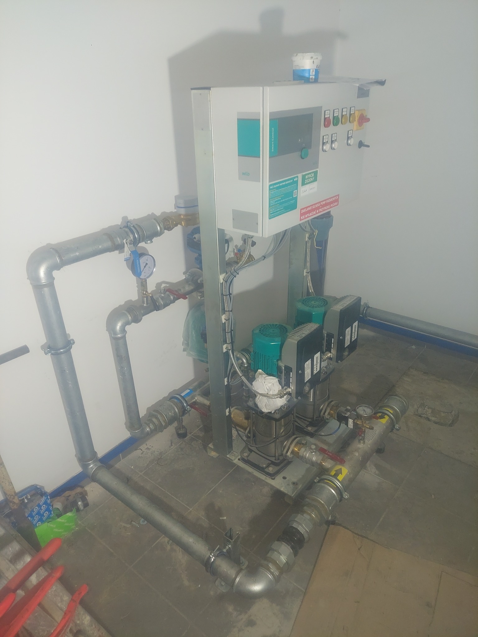 Kompletna instalacja pompowa Wilo w pomieszczeniu technicznym, z widocznymi rurami, manometrami i panelem sterowania z przyciskami.