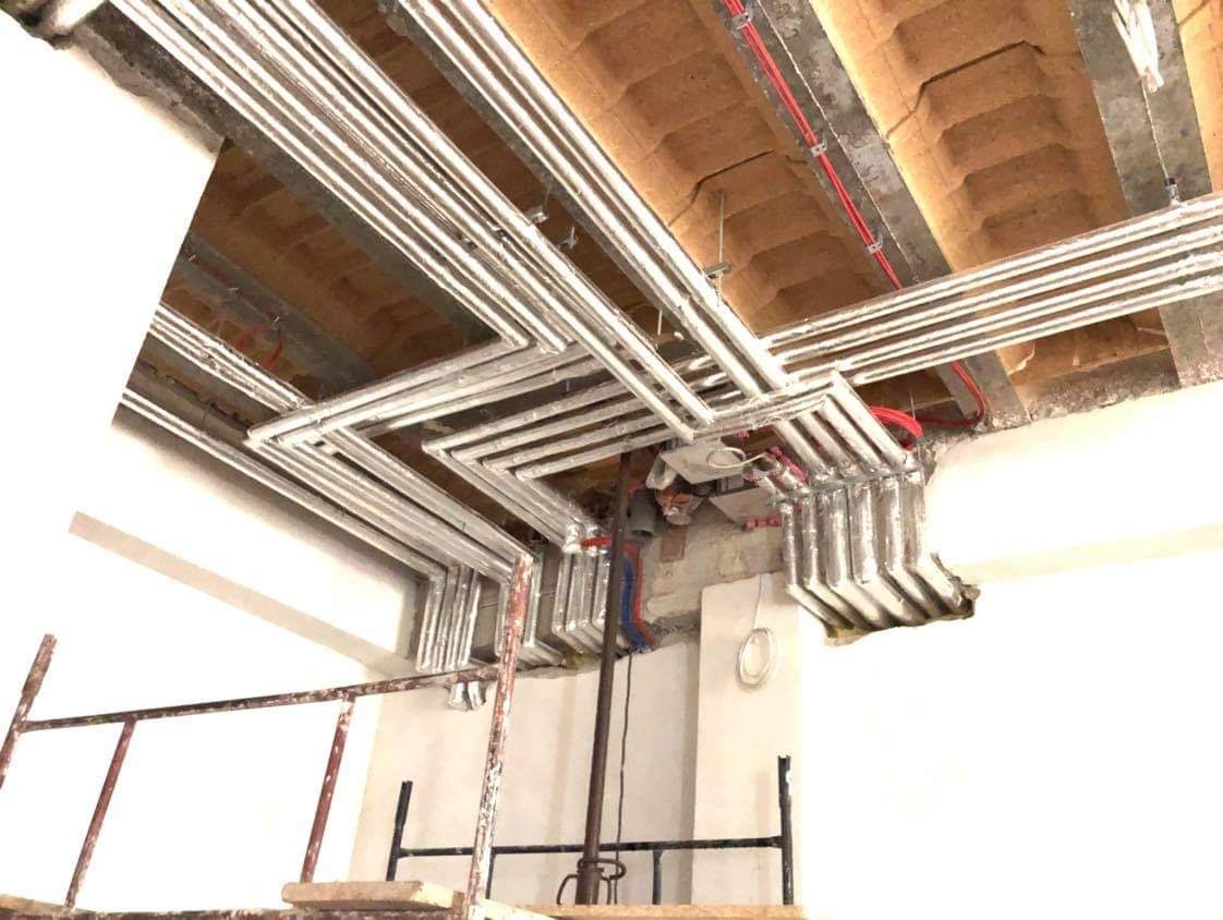 Skomplikowany układ rur instalacji w surowym wnętrzu, widok z rusztowania, instalacja elektryczna w czerwonej osłonie.