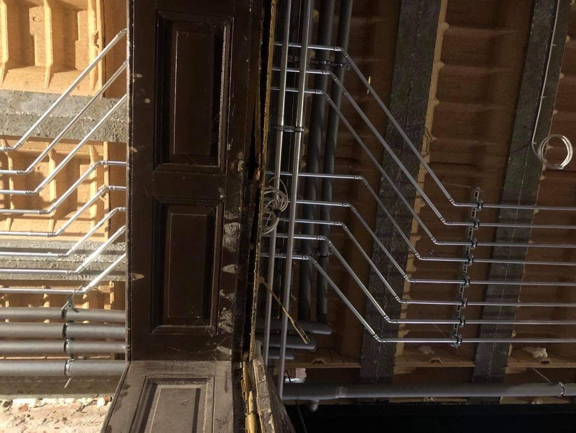 Szczegółowe ujęcie instalacji rur w pomieszczeniu w trakcie remontu, widoczne drewniane elementy konstrukcyjne i stara, ciemna futryna drzwiowa.