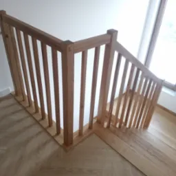 Fragment drewnianej balustrady schodowej z pionowymi szczebelkami i drewnianej podłogi ułożonej w jodełkę, widok z góry.