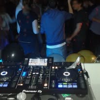 Konsoleta DJ Pioneer Dj na tle tańczących osób w słabym oświetleniu, widoczny fragment balonów i mikrofon.