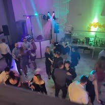 Zespół muzyczny grający na żywo podczas imprezy, widoczni tancerze i oświetlenie sceniczne w kolorach fioletu i zieleni.