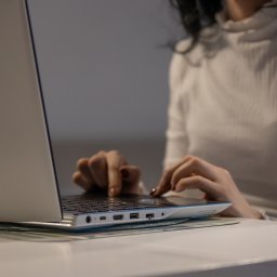 Wojciech Polański - Kobieta w białej bluzce pisze na laptopie z niebieskimi akcentami, umieszczonym na zielonej podkładce na białym stole.