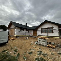 MODERN THERMO BUILDINGS SPÓŁKA Z OGRANICZONĄ ODPOWIEDZIALNOŚCIĄ - Budowa domu jednorodzinnego w trakcie ocieplania elewacji, widoczne rusztowania, materiały budowlane i samochód dostawczy Renault Trafic na tle pochmurnego nieba.