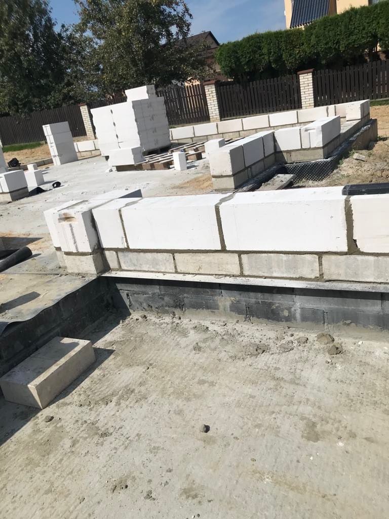 Wznoszenie ścian fundamentowych z bloczków betonowych na przygotowanym terenie budowy domu jednorodzinnego, widoczne ułożone warstwy bloczków i zapas materiału budowlanego.