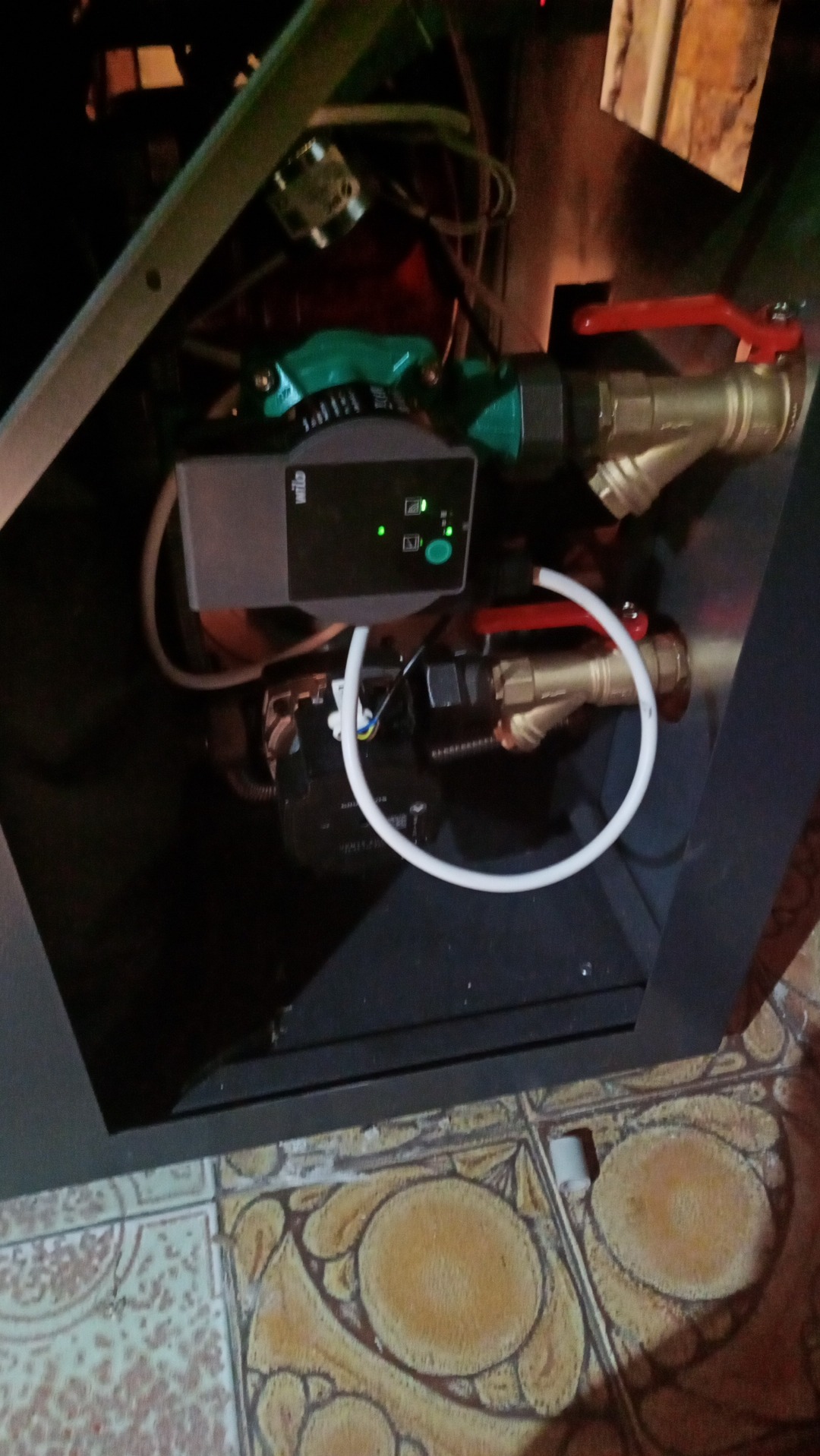 Fragment instalacji grzewczej w kotłowni z widoczną pompą obiegową Wilo z zielonymi diodami LED, zaworami kulowymi z czerwoną rączką i białym przewodem.