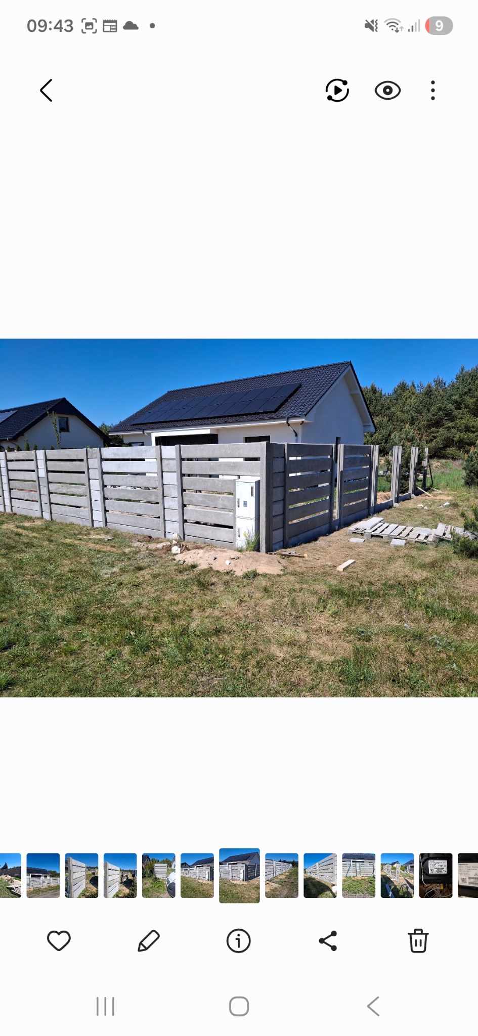 Nowoczesne ogrodzenie betonowe z poziomymi przęsłami, częściowo zamontowane. Widoczne elementy montażowe i skrzynka elektryczna. Trawa i dom w tle.