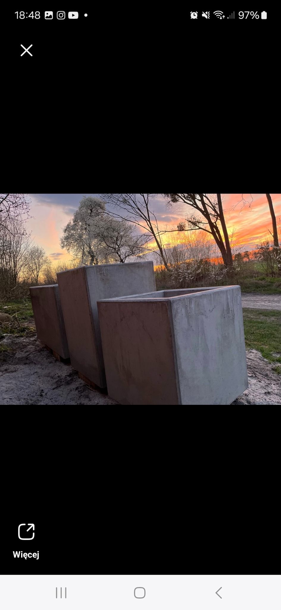 Trzy betonowe donice w kształcie sześcianów na zewnątrz, z widocznym zachodem słońca w tle, tworzące minimalistyczny element dekoracyjny ogrodu.