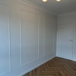 Jasne wnętrze z panelami ściennymi w stylu angielskim, parkietem w jodełkę i nowoczesną lampą sufitową.