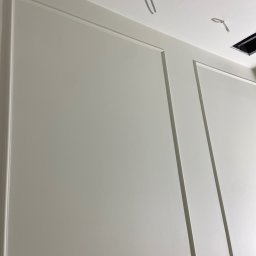 Wykończenia Wnętrz Mateusz Cirocki - Pomalowana na biało ściana z dekoracyjnymi listwami w stylu klasycznym, widoczne wystające przewody elektryczne i otwór w suficie.