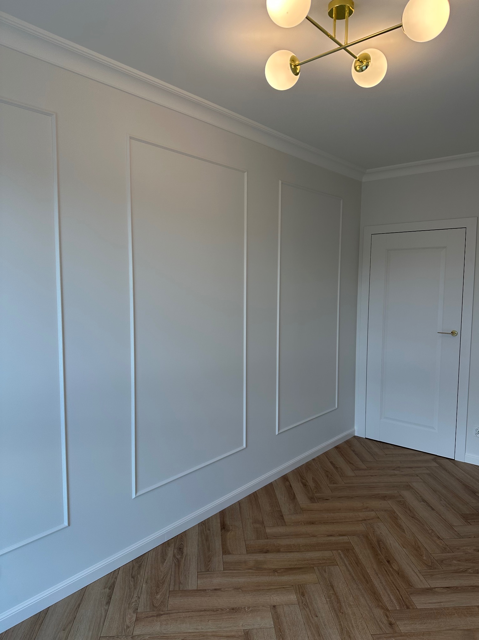 Jasne wnętrze z panelami ściennymi w stylu angielskim, parkietem w jodełkę i nowoczesną lampą sufitową.