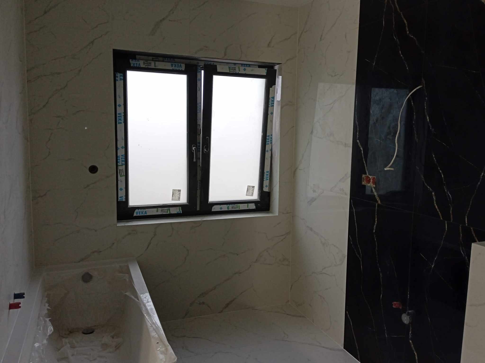 Wykończona łazienka w Sulechowie z biało-czarnymi marmurowymi płytkami, widoczna wanna częściowo zakryta folią ochronną oraz okno z czarną ramą.