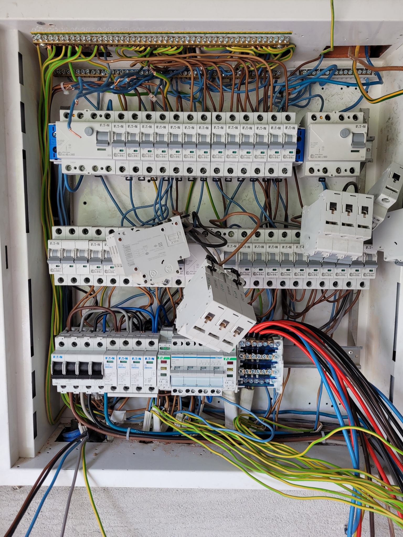 Otwarta skrzynka z bezpiecznikami i przewodami w różnych kolorach. Widoczne liczne zabezpieczenia marki Eaton. Niektóre przewody odłączone.