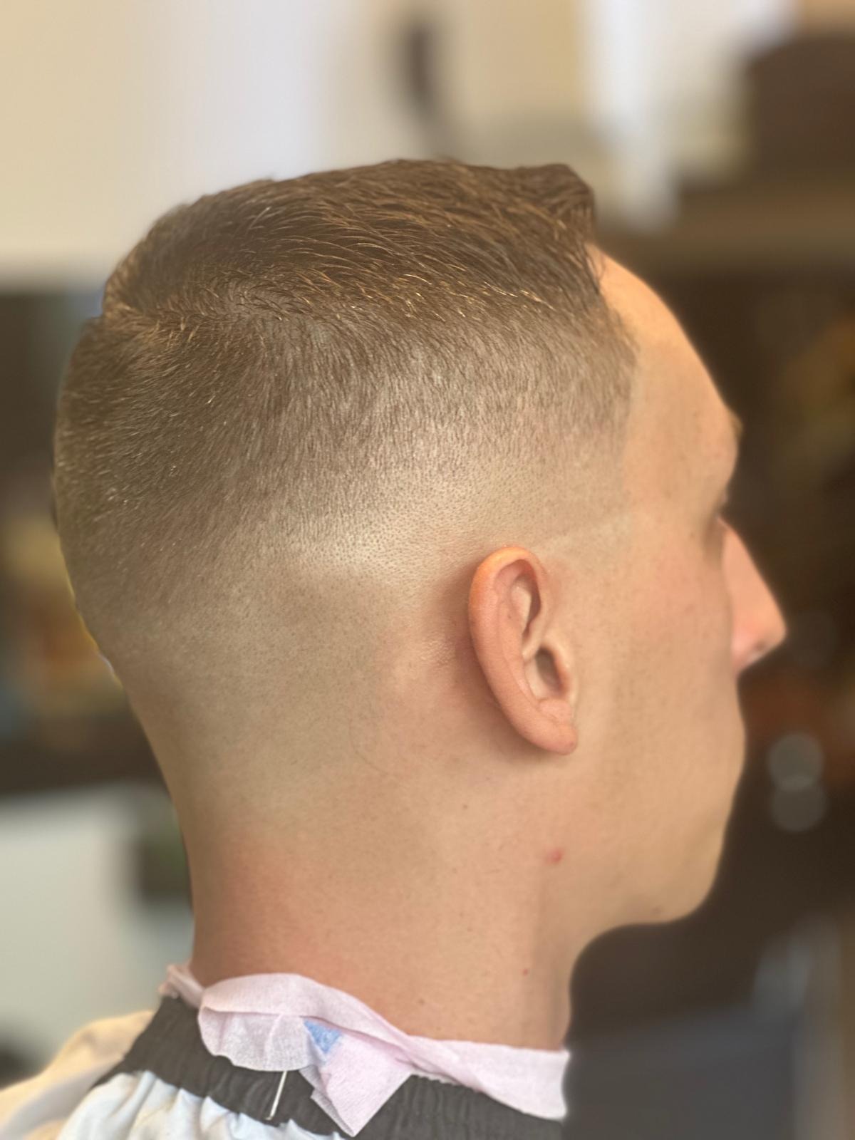 Męskie strzyżenie z wyraźnym cieniowaniem na bokach i karku, widoczne z profilu, z papierowym kołnierzem ochronnym.