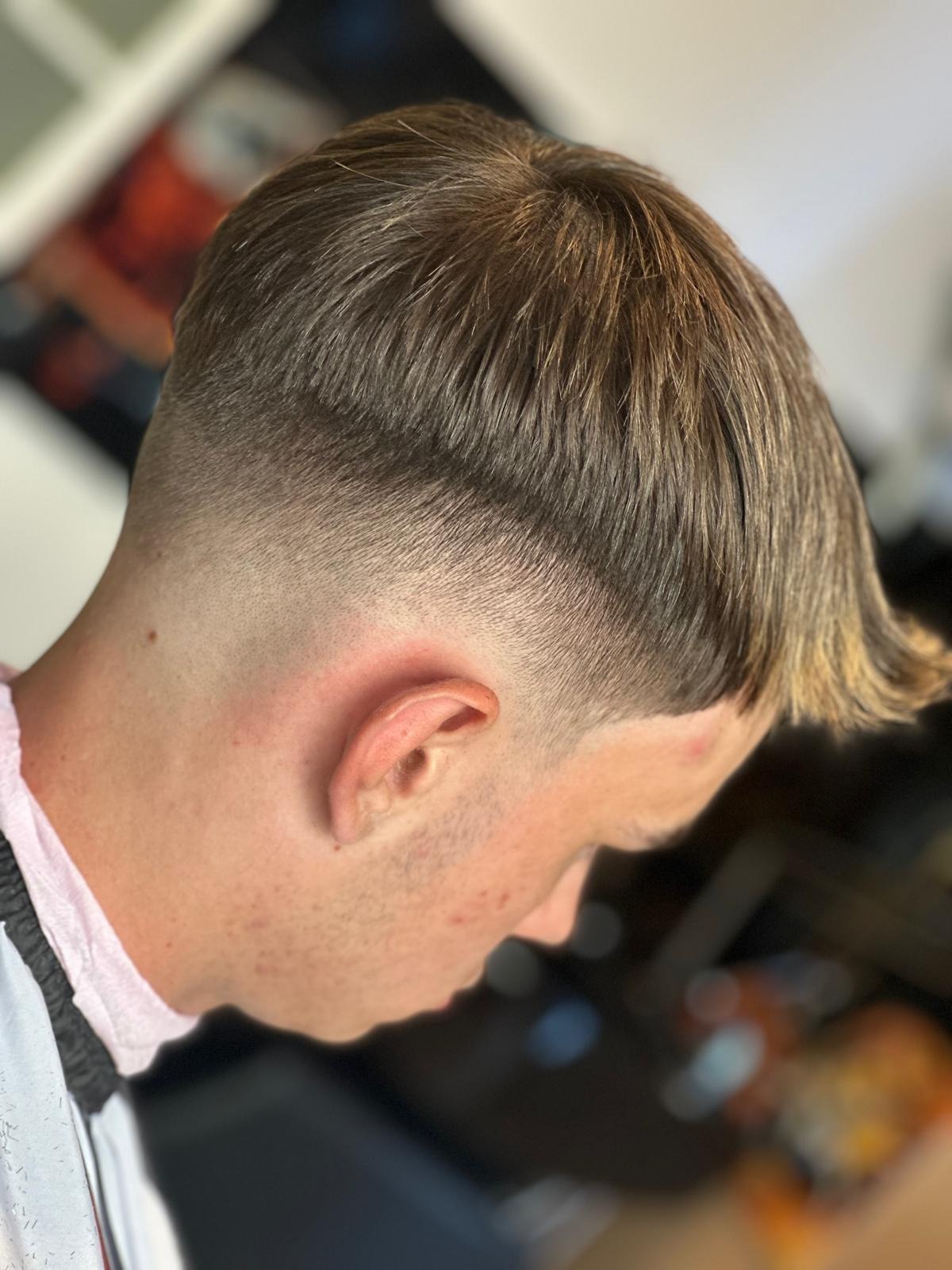 Męska fryzura z krótkimi bokami i dłuższymi, blond końcówkami, widok z tyłu głowy i profilu twarzy.