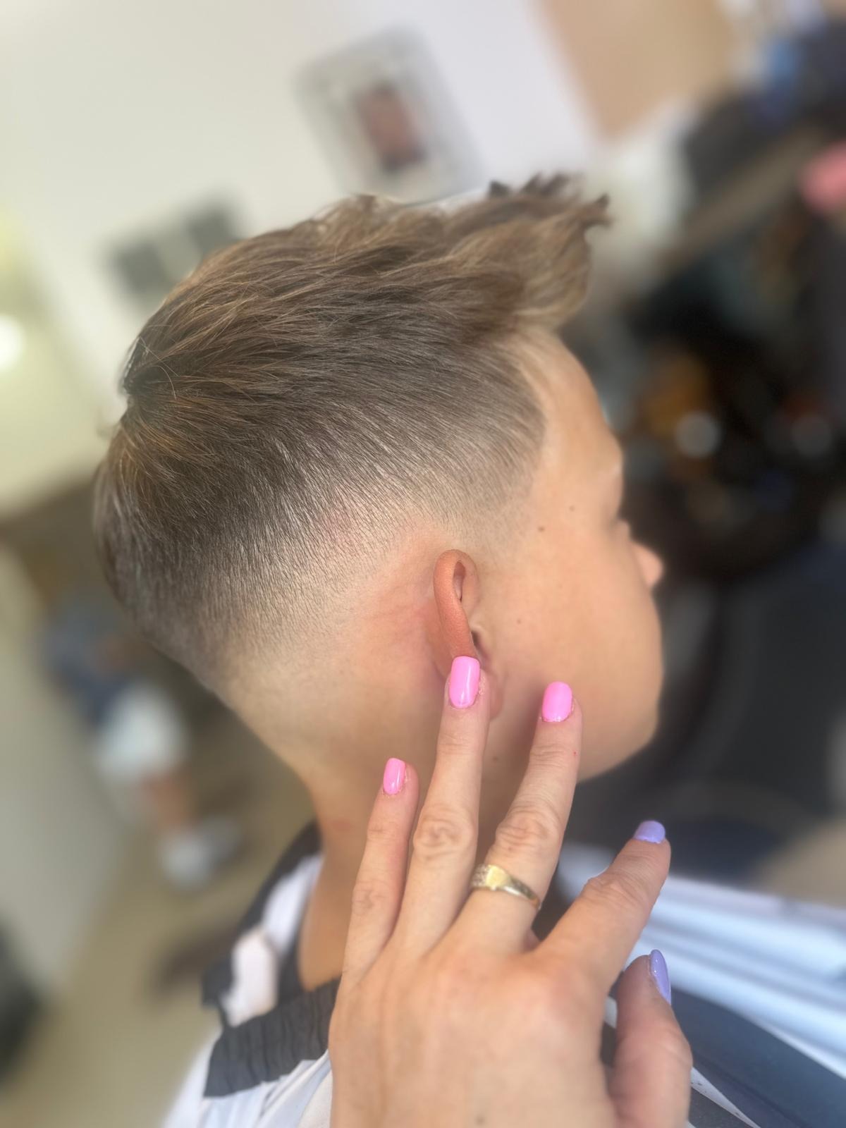 Włosy po strzyżeniu męskim z wycieniowanym bokiem, z bliska widoczna dłoń z pomalowanymi paznokciami w odcieniach różu i fioletu.