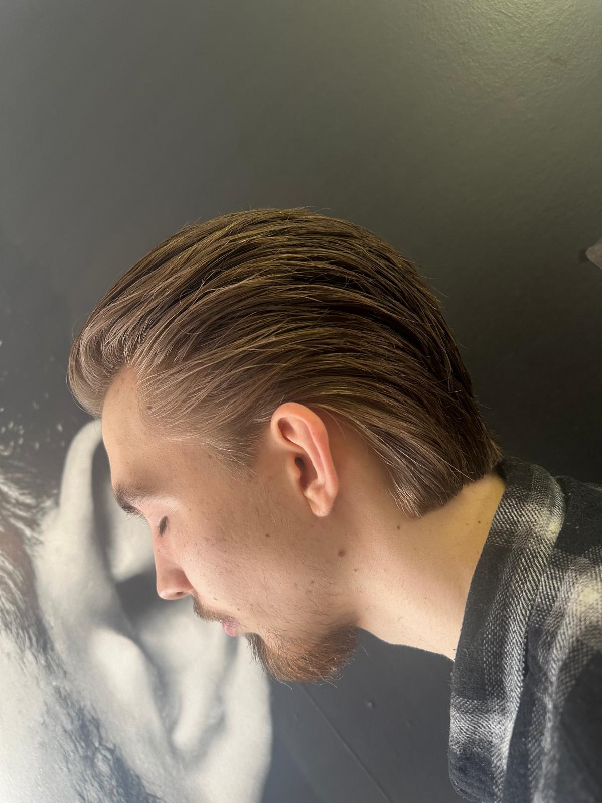 Męskie włosy po strzyżeniu, zaczesane do tyłu, widoczny profil twarzy modela z lekkim zarostem na tle grafiki na ścianie.