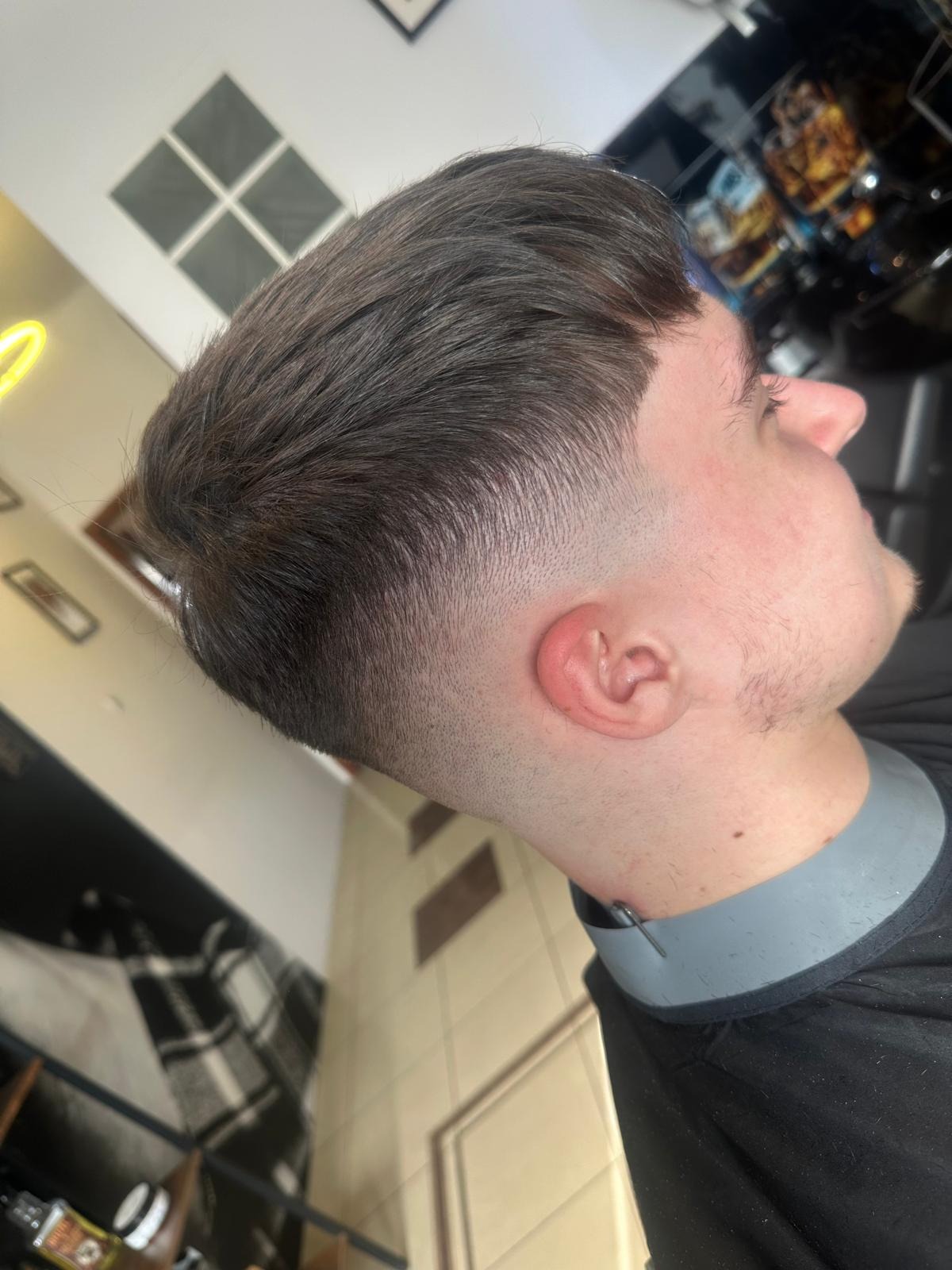 Męskie cięcie włosów z wyraźnym cieniowaniem, widoczne z profilu, z ochronnym kołnierzem na szyi.